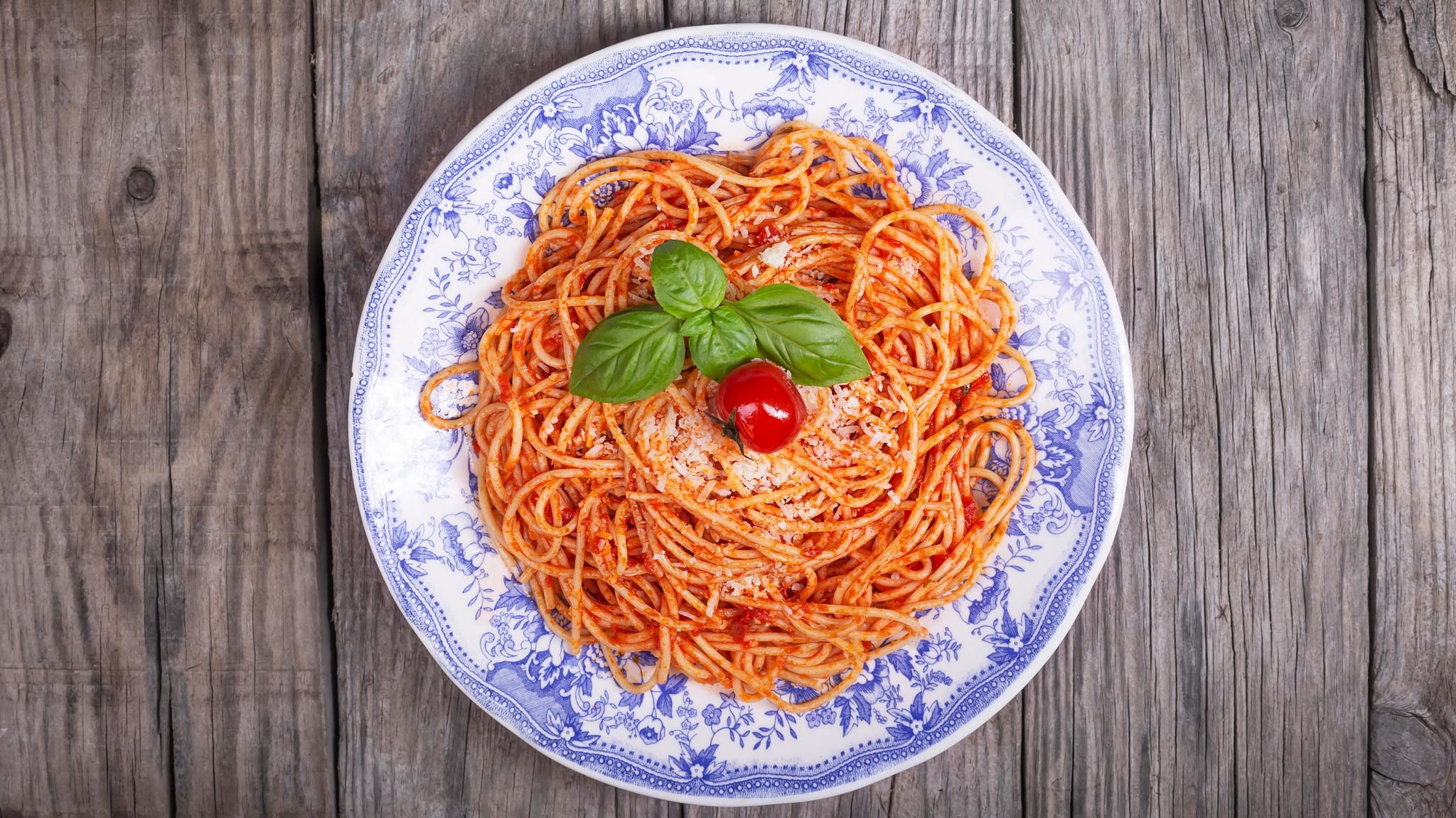 Alberto Grandi: Ein blau gemusterter Teller Pasta mit Tomatensauce, Basilikum und Parmesan auf einem Holztisch