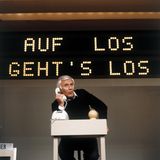 Joachim Fuchsberger an einem Schreibtisch, er hält sich einen Telefonhörer ans Ohr und spricht mit jemandem