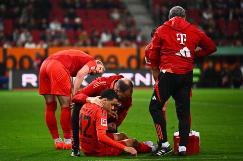 Bayern Münchens Jamal Musiala sitzt verletzt am Boden und wird von Mannschaftsarzt Dr. Jochen Hahne behandelt