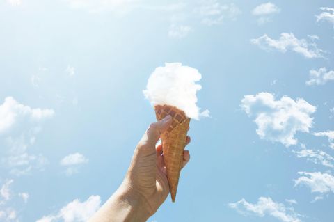 Hoffnung: eine Hand hält eine Eiswaffel mit einer Kugel aus einer Wolke in die Luft