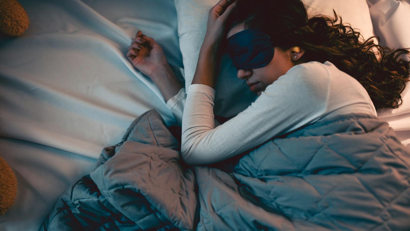 Frau im Bett mit Schlafmaske und Ohrenstöpseln