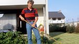 Rudi Völler mit Harke in seinem Garten, er trägt Jeans und gestreiftes Polohemd