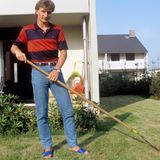Rudi Völler mit Harke in seinem Garten, er trägt Jeans und gestreiftes Polohemd