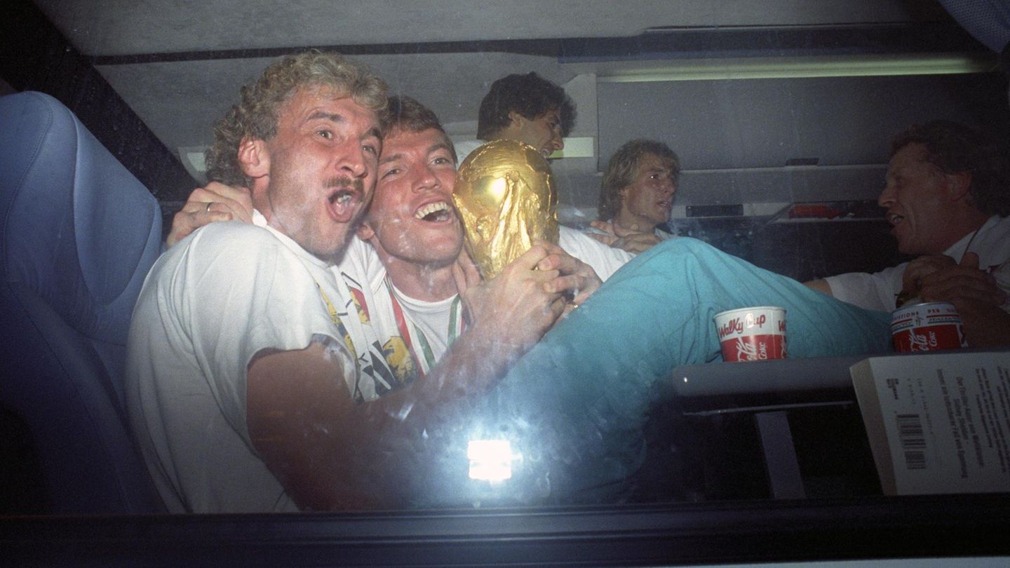 Rudi Völler und Lothar Matthäus sitzen im Mannschaftsbus und halten den WM-Pokal fest