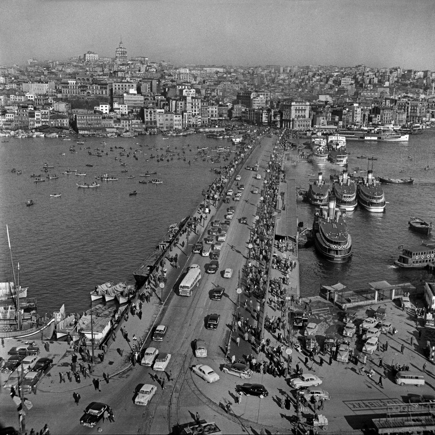 Uralt sind die Wurzeln Istanbuls. Über die Jahrtausende trägt die Stadt verschiedene Namen, erlebt römische, byzantinische und schließlich osmanische Herren, bis sie 1923 zur größten Metropole der türkischen Republik wird, wenn auch nicht zu ihrer Kapitale. Auch die Galatabrücke über das Goldene Horn hat eine lange Geschichte: Zu Zeiten der Osmanenherrschaft errichtet, wird sie mehrmals erneuert – und ist 1958, als diese Aufnahme entsteht, eine enorm wichtige Verkehrsader