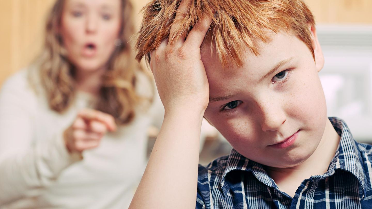 Eine Junge fasst sich an den Kopf, die Mutter hinter ihm schimpft