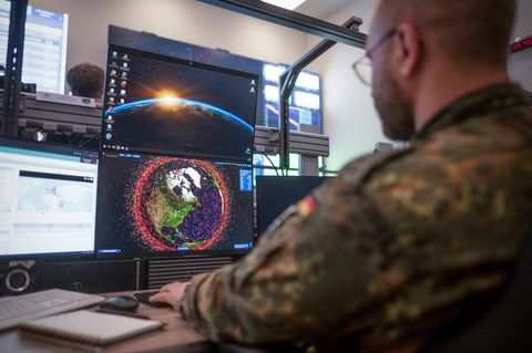 Soldat der Bundeswehr vor Monitor mit Satellitebahnen