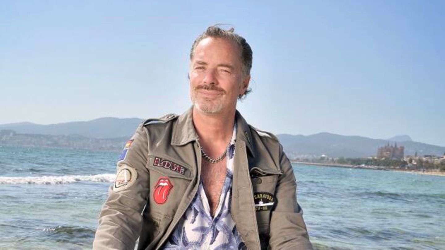 John Friedmann sitzt mit überkreuzten Beinen auf einem Stein am Strand von Palma de Mallorca