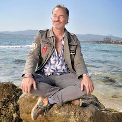 John Friedmann sitzt mit überkreuzten Beinen auf einem Stein am Strand von Palma de Mallorca