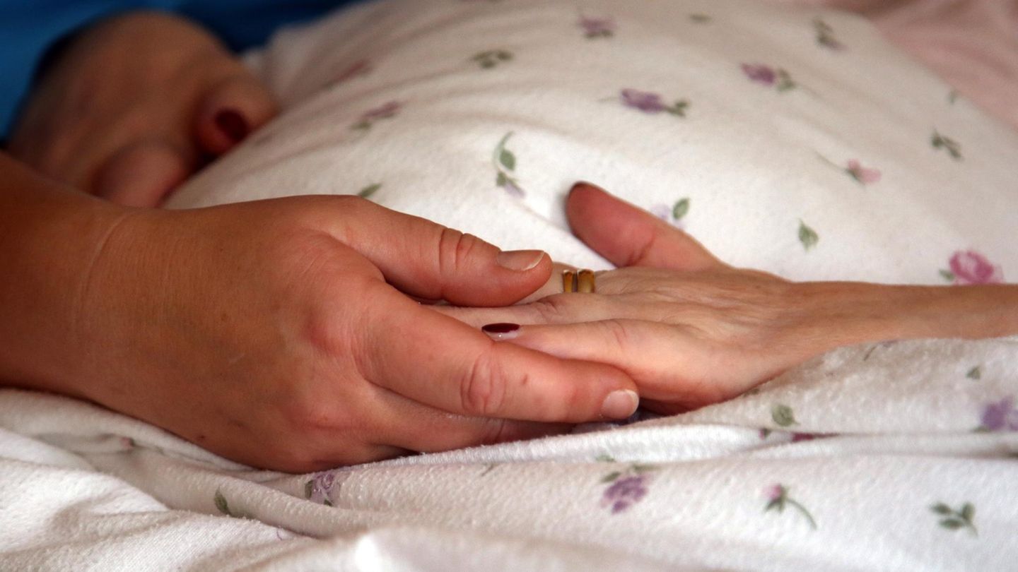 Die Hände einer Bewohnerin liegen in einem Hospiz auf einer Bettdecke