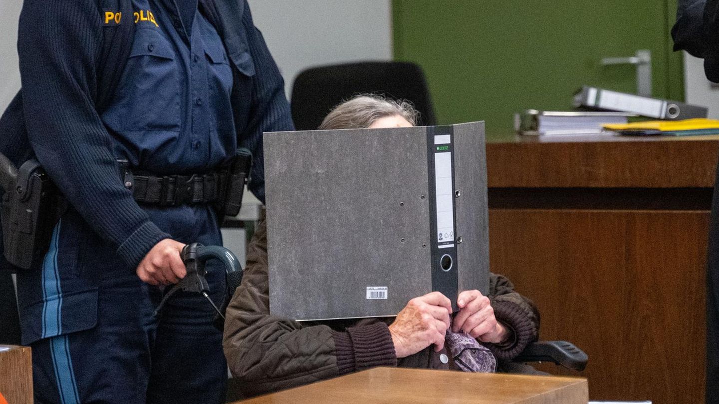 Die angeklagte Seniorin wird von einer Polizistin in einem Rollstuhl in einen Sitzungssaal im Landgericht München I geschoben