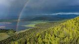 Im Hintergrund ein See, vorne Wald und ein Regenbogen