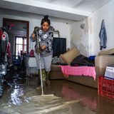 Eine Frau versucht mit einem Besen die Wassermassen zu beseitigen