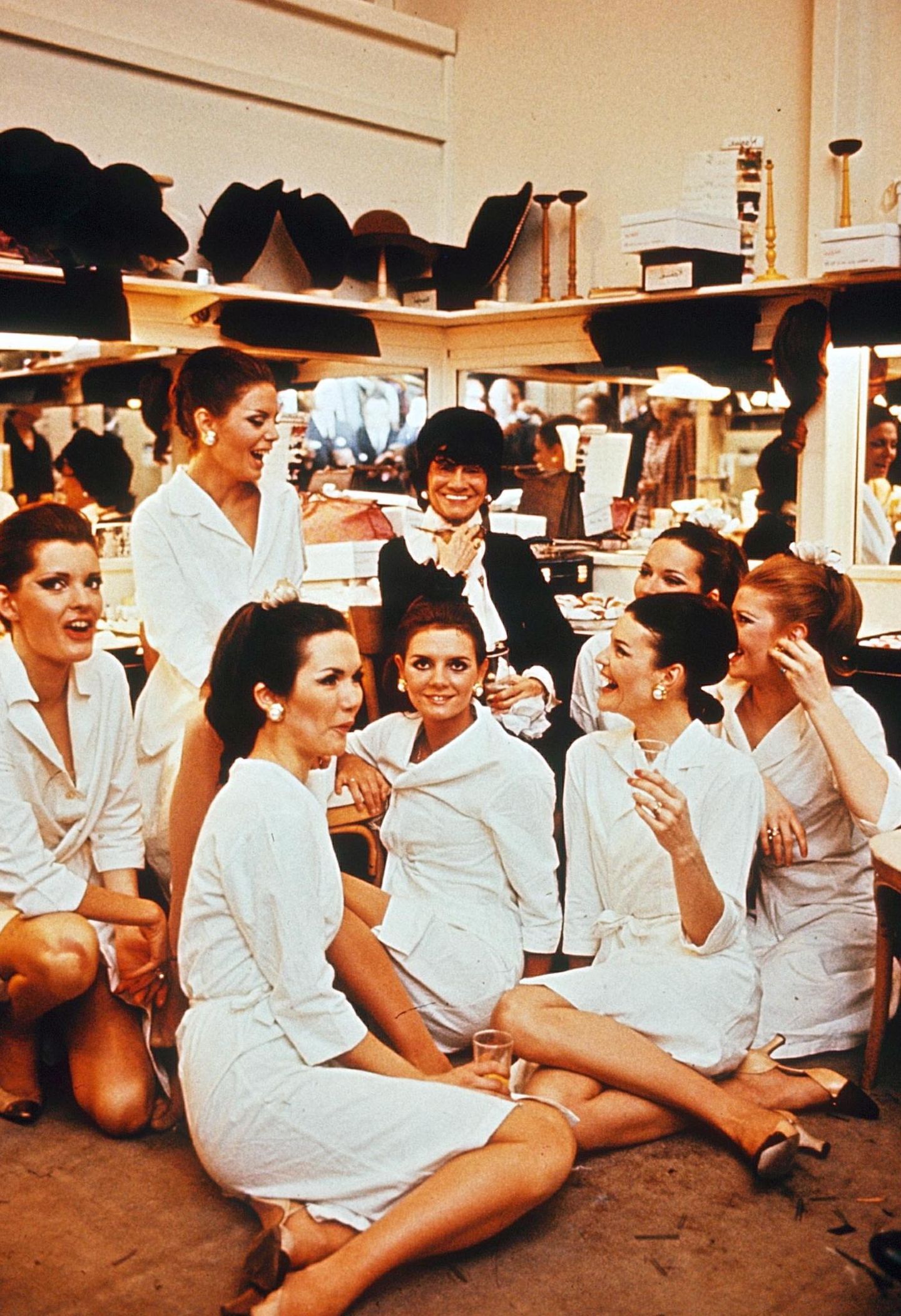 Coco Chanel in den 60er-Jahren im Kreise ihrer Mitarbeiterinnen. Im Hintergrund Regale mit Hüten