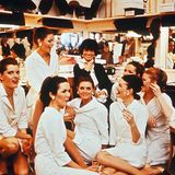 Coco Chanel in den 60er-Jahren im Kreise ihrer Mitarbeiterinnen. Im Hintergrund Regale mit Hüten