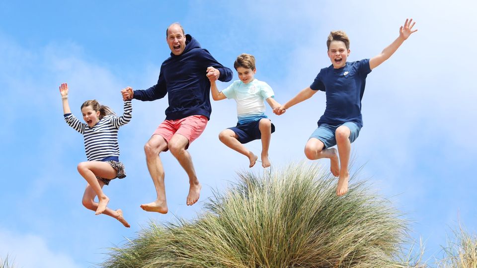 Prince William and his children - on the right of him Prince Louis - jump from a dune
