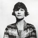 Ein Portrait von Coco Chanel, sie verschränkt die Arme vor dem Körper