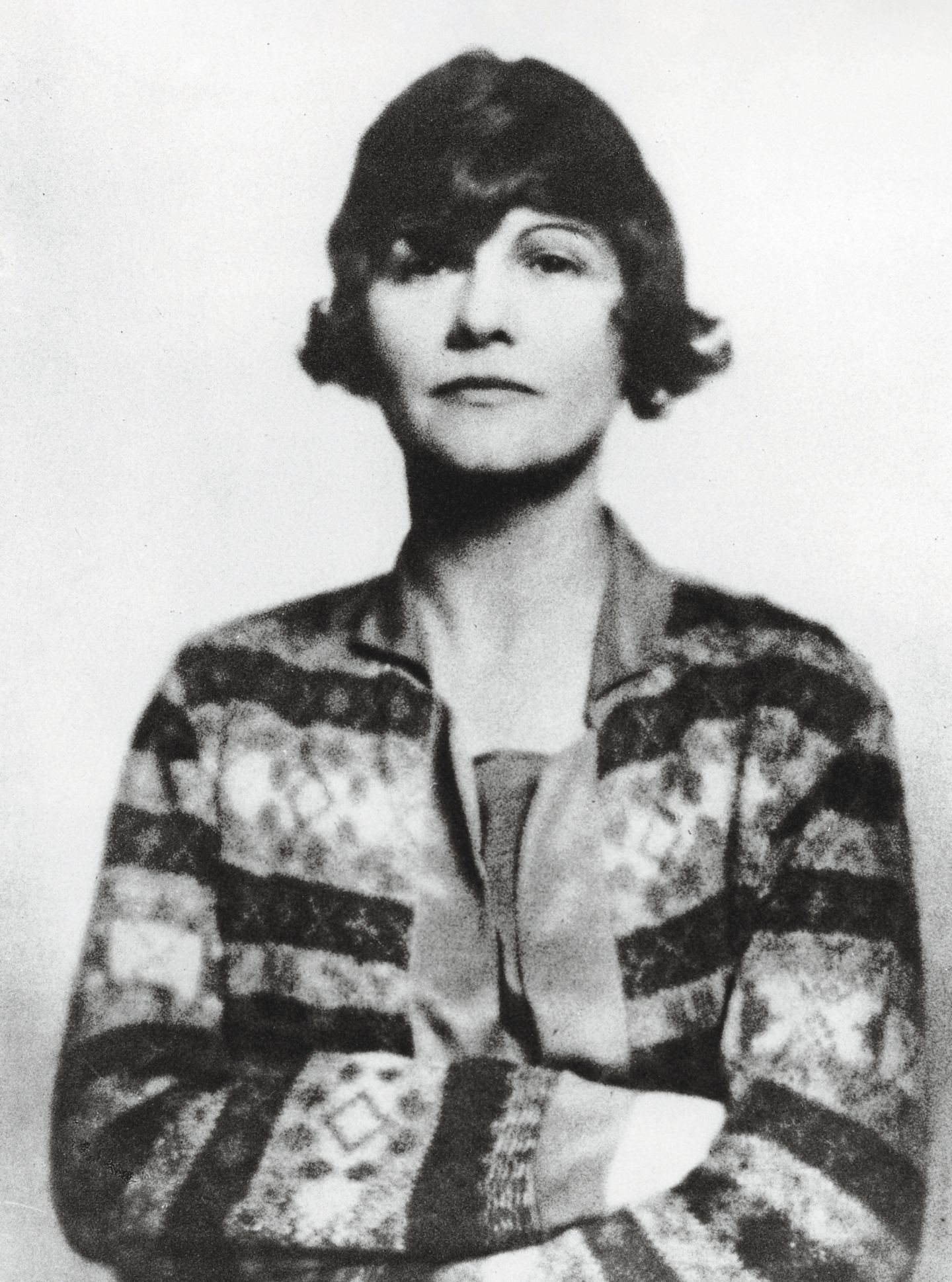 Ein Portrait von Coco Chanel, sie verschränkt die Arme vor dem Körper