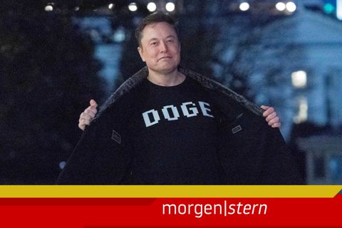 Elon Musk öffnet seinen Blazer, auf dem T-Shirt darunter steht "Doge" geschrieben