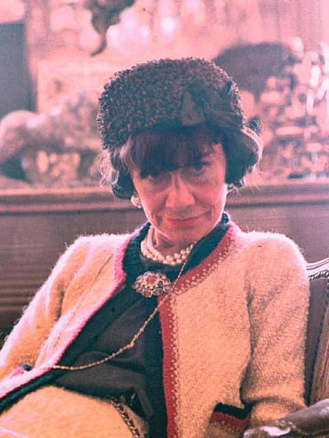 Coco Chanel 1965, sie trägt einen schwarzen Hut und eine weiße Chanel-Jacke