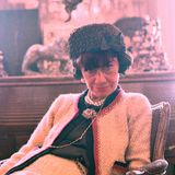 Coco Chanel 1965, sie trägt einen schwarzen Hut und eine weiße Chanel-Jacke