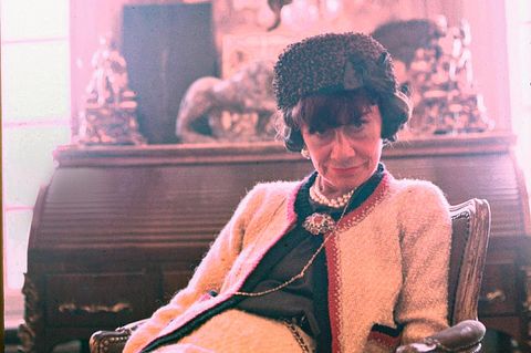 Coco Chanel 1965, sie trägt einen schwarzen Hut und eine weiße Chanel-Jacke