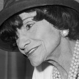 Im Portrait: Coco Chanel mit schwarzem Hut, weißen Perlenohrringen und Perlenketten