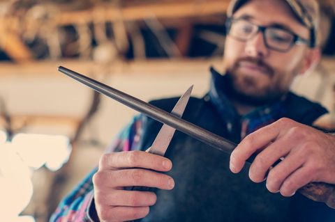 Low angle view of male taxidermist sharpening knife at workshop