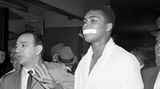 Muhammad Ali im weißen Bademantel, er hat sich ein Stück weißes Tape vor den Mund geklebt