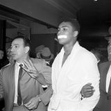 Muhammad Ali im weißen Bademantel, er hat sich ein Stück weißes Tape vor den Mund geklebt