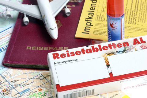 Ein Reisepass, ein Spielzeugflugzeug, Anti-Zeckenspray, ein Impfpass und Reisetabletten liegen eng beieinander