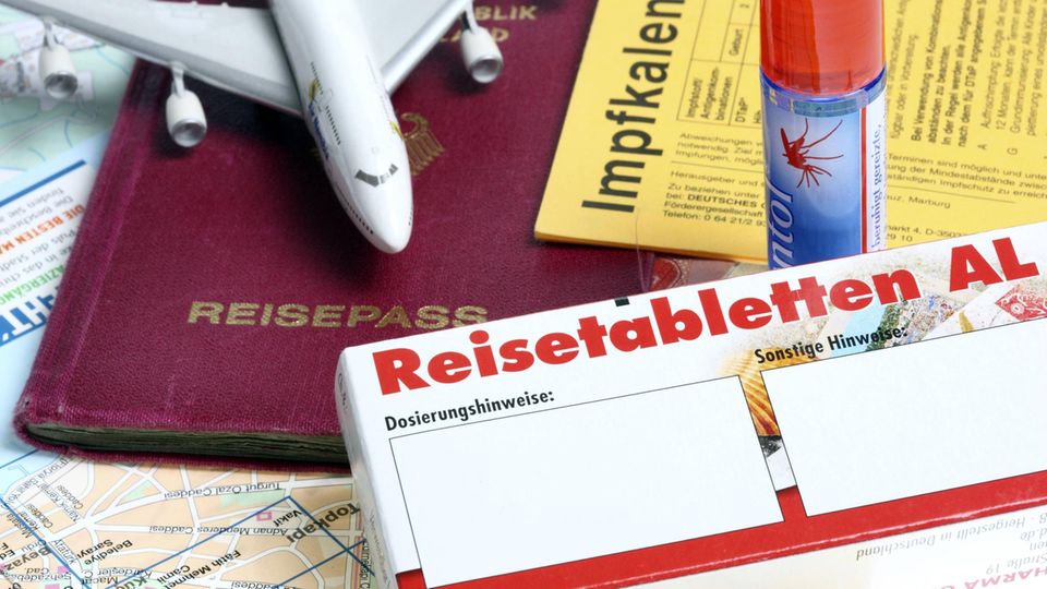 Keine Tabletten mehr? Dieses Geräusch soll gegen Reiseübel Ein Reisepass, ein Spielzeugflugzeug, Anti-Zeckenspray, ein Impfpass und Reisetabletten liegen eng beieinander