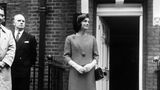 Jackie Kennedy stehend im Kostüm mit einer schwarzen Chanel-Handtasche über. dem linken Arm