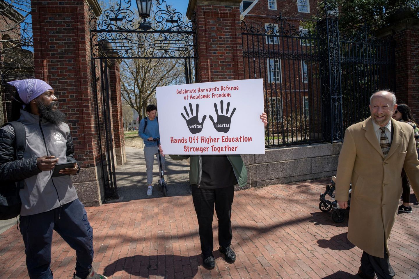 vier Menschen vor der Harvard Universität von denen einer ein Schild hochhält