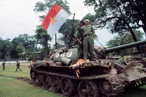 Nordamerikanische Soldaten stehen auf einem Panzer und hissen die Flagge des Vietcong