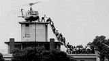 Helikopter steht auf Dach eines Gebäudes, Menschen klettern über eine schmale Treppe zu dem Helikopter
