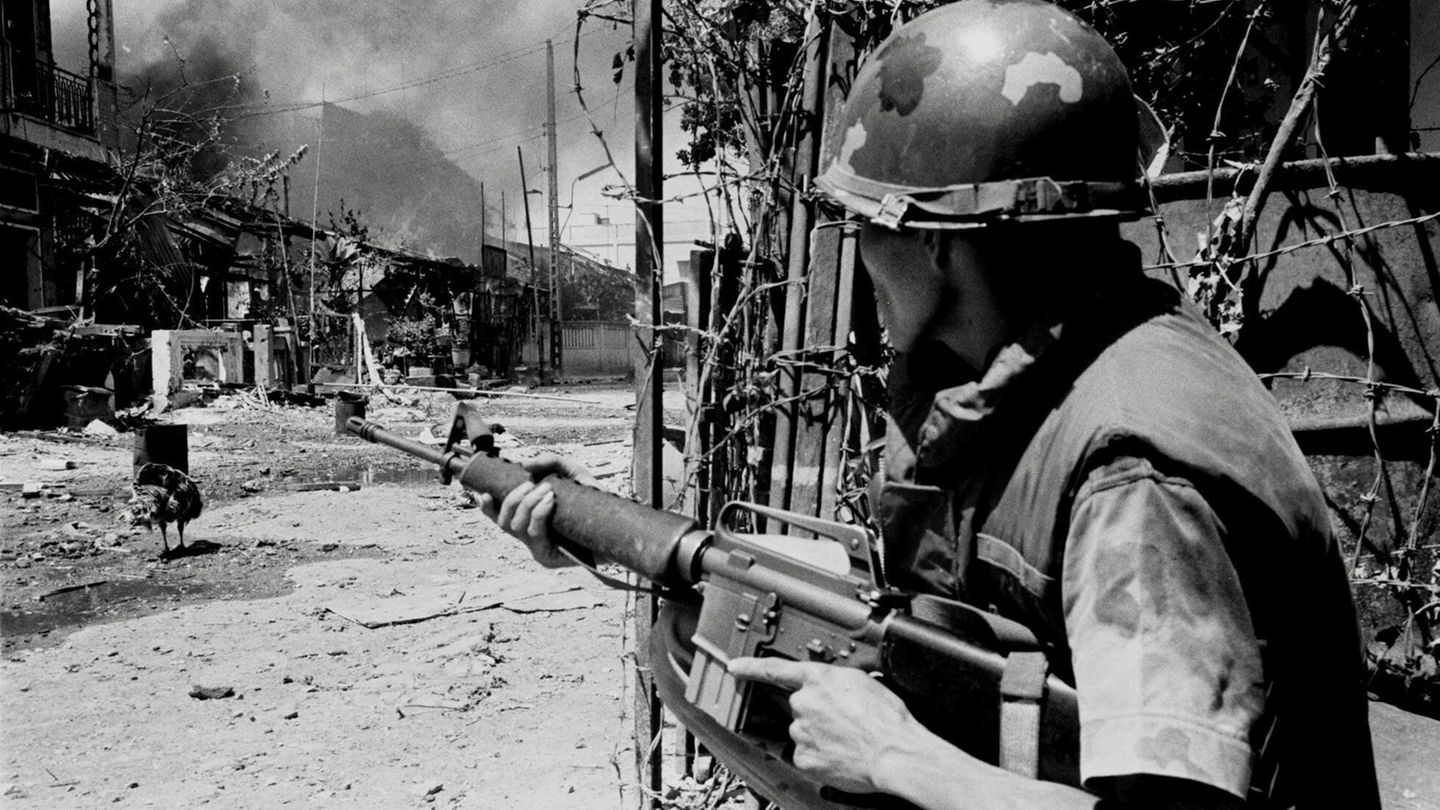 Soldat versteckt sich hinter einer Wand und schaut auf eine verwüstete Straße Soldat versteckt sich hinter einer Wand und schaut auf eine verwüstete Straße
