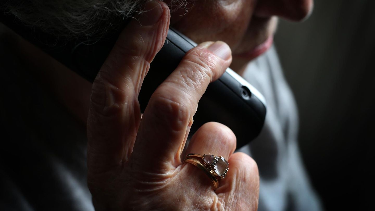 Eine ältere Frau mit einem Ring am Finger hält sich den Telefonhörer ans Ohr / Bebilderung zum Thema Falsche Polizisten
