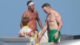 David Beckham mit nacktem Oberkörper und Stirnband auf einer Yacht, links und rechts von ihm Elton John und Mann