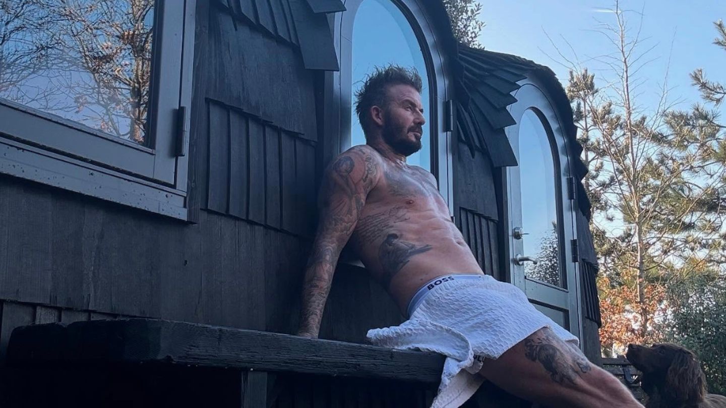 David Beckham sitzt vor einer Sauna, nur ein Handtuch um die Taille