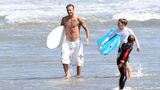 David Beckham in langer weißer Badehose und mit Surfbrett unterm Arm – so kommt er aus dem Wasser