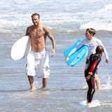 David Beckham in langer weißer Badehose und mit Surfbrett unterm Arm – so kommt er aus dem Wasser