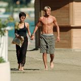 David Beckham in langer Badehose Hand in Hand mit Ehefrau Victoria im schwarzen Kleid am Strand