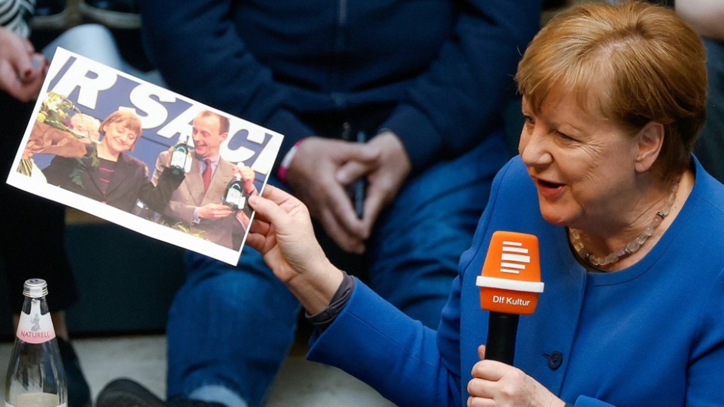Angela Merkel hält ein Bild von sich und Merz in der Hand