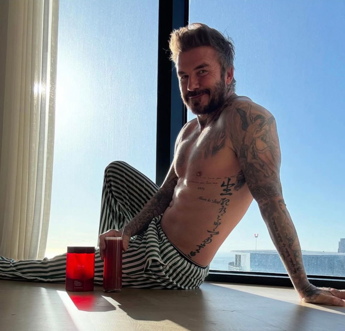 Guten Morgen! David Beckham, lange Schlafanzughose, nackter Oberkörper, sitzt in seinem Apartment in Miami vor einem Fenster