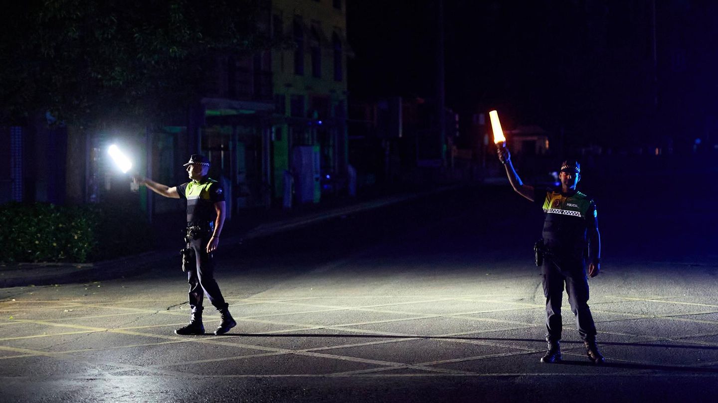 Zwei Polizisten auf der Straße halten während des Blackouts Lampen in der Hand – um sie rum ist alles finster Zwei Polizisten auf der Straße halten während des Blackouts Lampen in der Hand – um sie rum ist alles finster