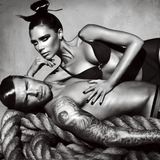 David Beckham liegend, seine Frau Victoria schmiegt sich an ihn. Beide tragen schwarze Unterwäsche