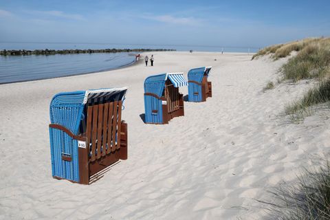 Drei blaue Strandkörbe stehen bei schönstem Wetter am Rand einer Düne