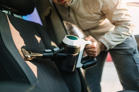 Man Using Portable Vacuum Cleaner to Clean Interior of Vehicle Seat