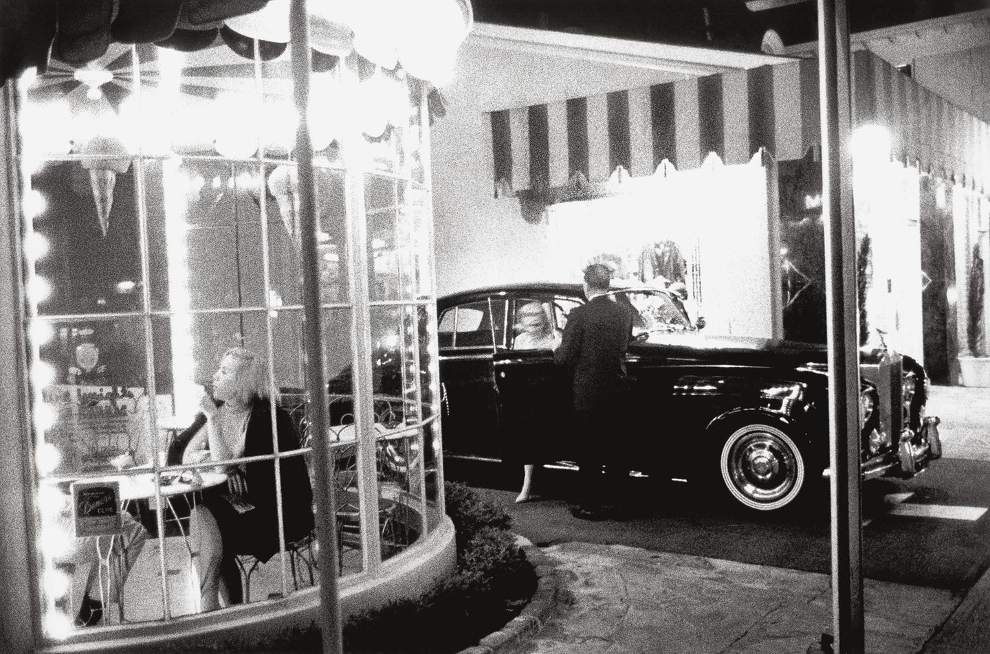 Blick in ein rundes Café, hinter dem eine Frau aus einem Rolls-Royce steigt